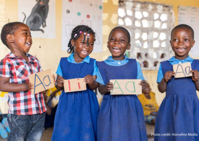 A boy and three girls laugh in primary school class as they learn how to write letters of the alphabet.