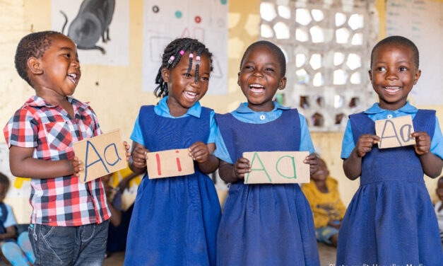 A boy and three girls laugh in primary school class as they learn how to write letters of the alphabet.