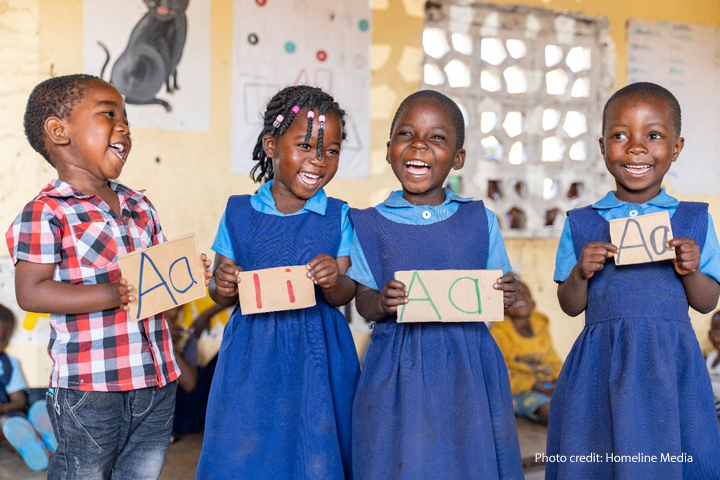 A boy and three girls laugh in primary school class as they learn how to write letters of the alphabet.