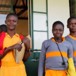 Three adolescent girls come out of their classroom at a PEAS school, Uganda