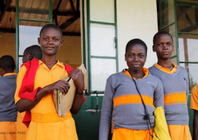 Three adolescent girls come out of their classroom at a PEAS school, Uganda