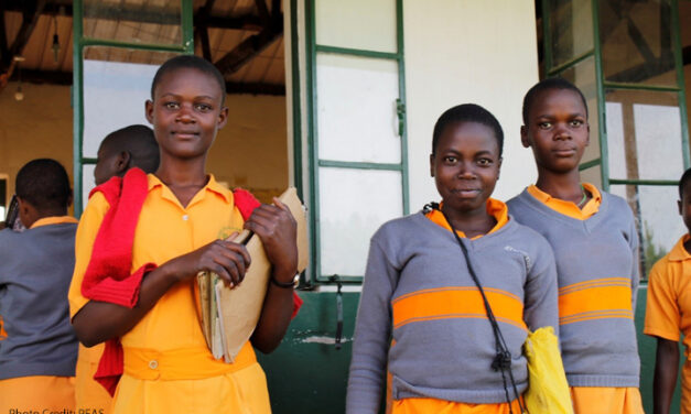 Three adolescent girls come out of their classroom at a PEAS school, Uganda