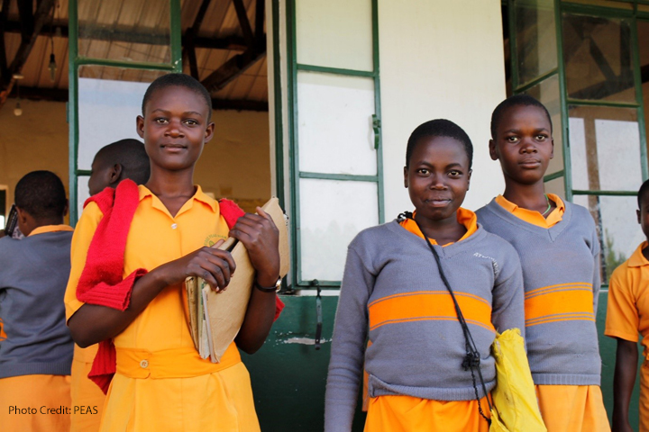 Three adolescent girls come out of their classroom at a PEAS school, Uganda