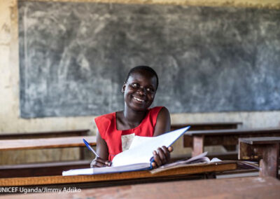 Faida, a teenage girl sits smiling in a classroom in Uganda after having been released from a child marriage after her husband kidnapped her.