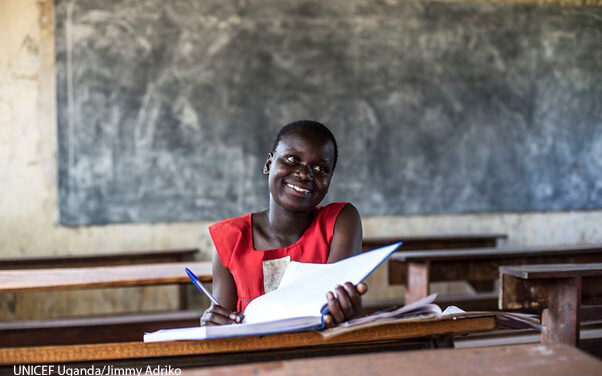 Faida, a teenage girl sits smiling in a classroom in Uganda after having been released from a child marriage after her husband kidnapped her.