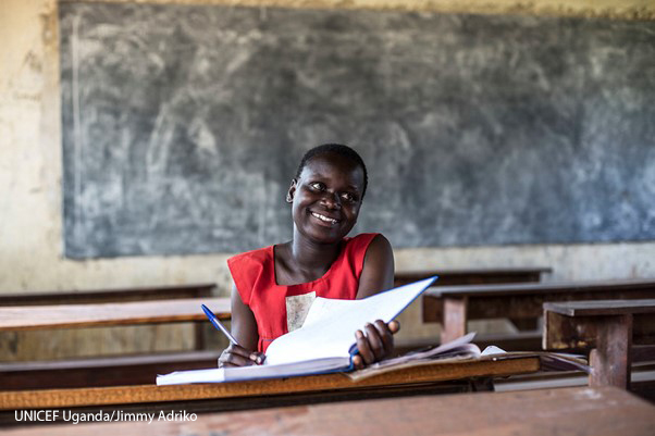 Faida, a teenage girl sits smiling in a classroom in Uganda after having been released from a child marriage after her husband kidnapped her.