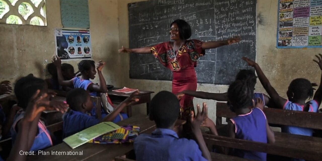 smiling teacher with her arms spread out in front of a class of children