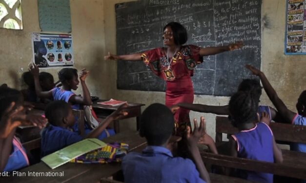 smiling teacher with her arms spread out in front of a class of children