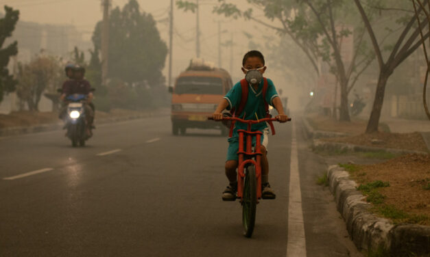 Boy in Thailand riding a moped in the smog with a face mask