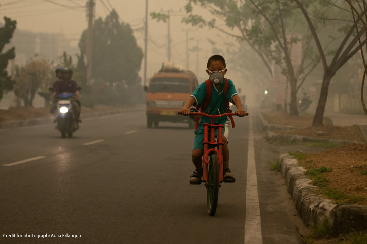 Boy in Thailand riding a moped in the smog with a face mask