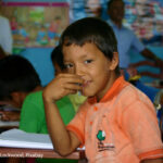 Boy sits at his desk in the classroom looking at the camera, Amazon jungle, Peru