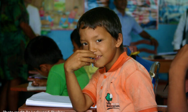 Boy sits at his desk in the classroom looking at the camera, Amazon jungle, Peru