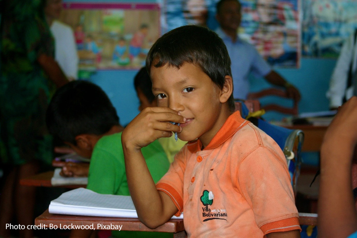 Boy sits at his desk in the classroom looking at the camera, Amazon jungle, Peru