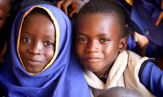 A young girl and boy smile at the camera in a classroom in Sierra Leone