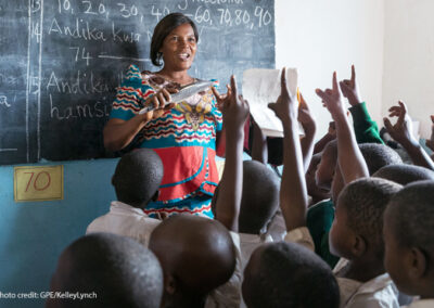 A female Standard 2 teacher teaches her class using locally made wooden teaching and learning materials (in this case a wooden fish), Kivukoni Primary School, Mpanda MC, Katavi, Tanzania.
