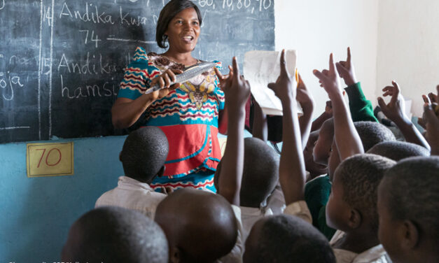 A female Standard 2 teacher teaches her class using locally made wooden teaching and learning materials (in this case a wooden fish), Kivukoni Primary School, Mpanda MC, Katavi, Tanzania.