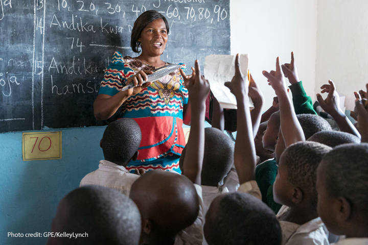 A female Standard 2 teacher teaches her class using locally made wooden teaching and learning materials (in this case a wooden fish), Kivukoni Primary School, Mpanda MC, Katavi, Tanzania.