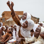 students try to get the teacher’s attention to answer a question, Sudan