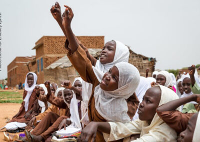 students try to get the teacher’s attention to answer a question, Sudan