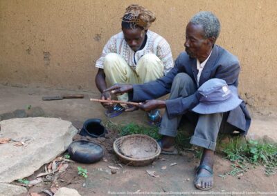 A senior rainmaker in the Nganyi community, Obedi Osore Nganyi (right), instructs Reuben Asitwa Okonda, an apprentice, on how to do the pot blowing. During the rainmaking activities, the rainmakers sometimes stay for hours or even days in the shrines and at this point it is normally the work of the assistant to keep them supplied with food and water.
