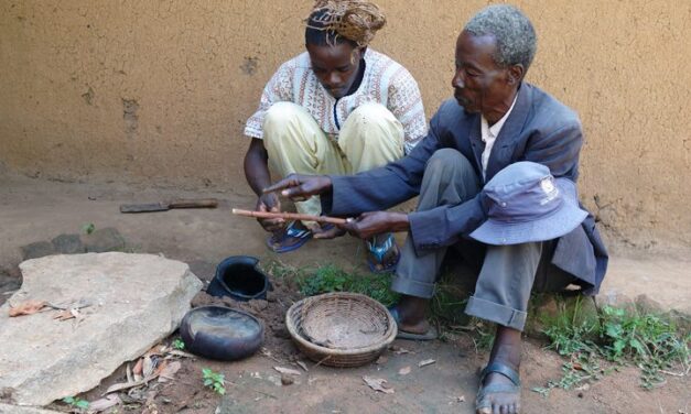 A senior rainmaker in the Nganyi community, Obedi Osore Nganyi (right), instructs Reuben Asitwa Okonda, an apprentice, on how to do the pot blowing. During the rainmaking activities, the rainmakers sometimes stay for hours or even days in the shrines and at this point it is normally the work of the assistant to keep them supplied with food and water.