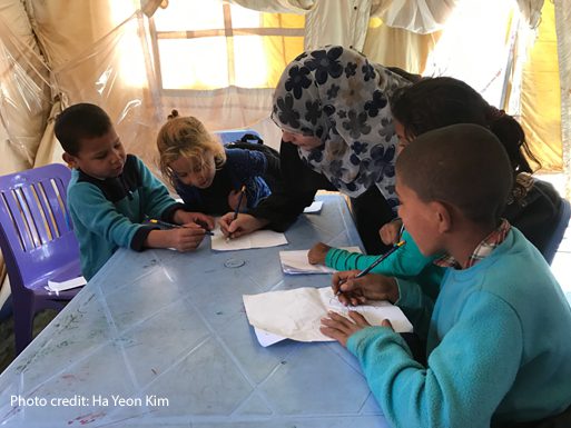 A group of Syrian children in IRC's remedial tutoring programme working together with their female teacher to learn how to write an Arabic letter,