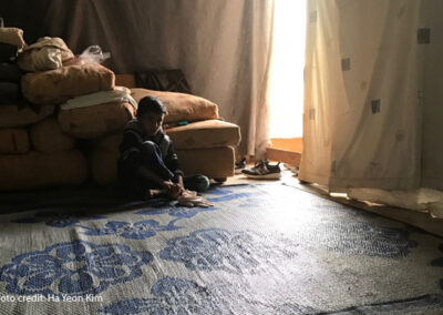 A Syrian refugee boy seated in a dimly-lit tent waiting his turn for social and emotional assessment