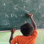 Young boy learns to write the letters of the alphabet with chalk on the blackboard of his primary school classroom, Somali Region, Ethiopia.
