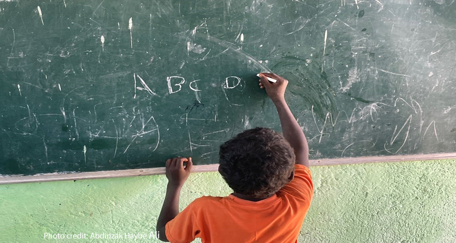 Young boy learns to write the letters of the alphabet with chalk on the blackboard of his primary school classroom, Somali Region, Ethiopia.