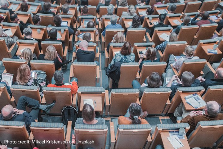 The back of tops of heads of students sitting in a university lecture theatre.