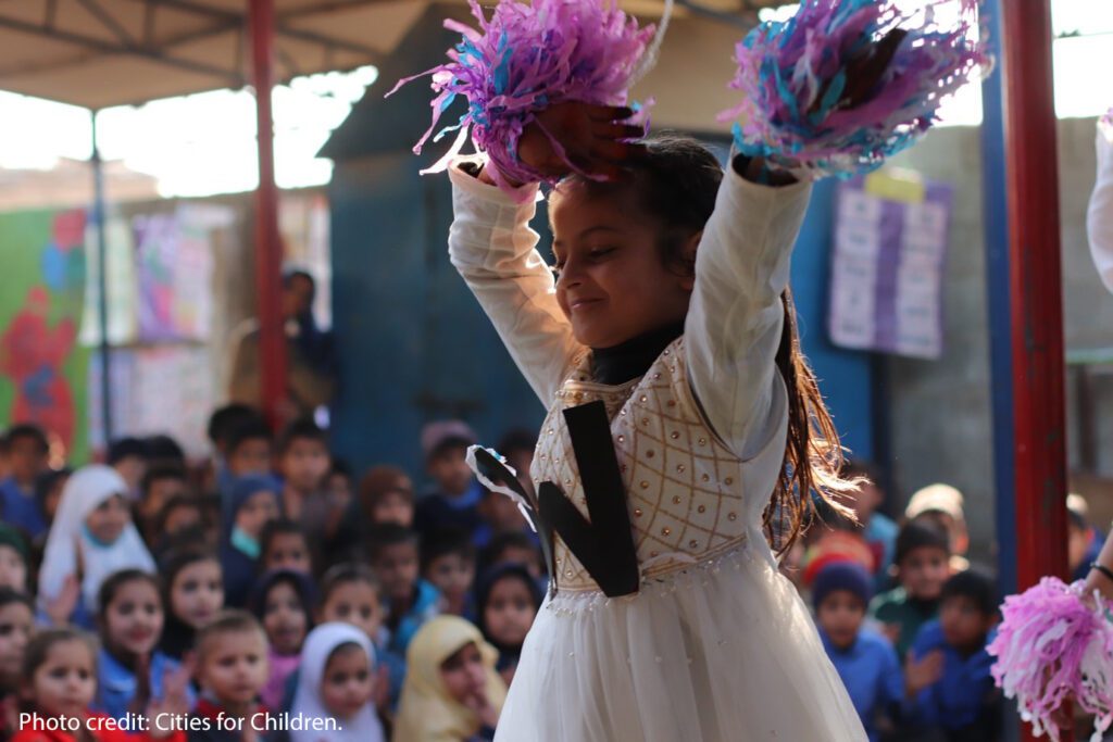 A girl dances as part of a group show with children watching, as part of a wellbeing exercise. 