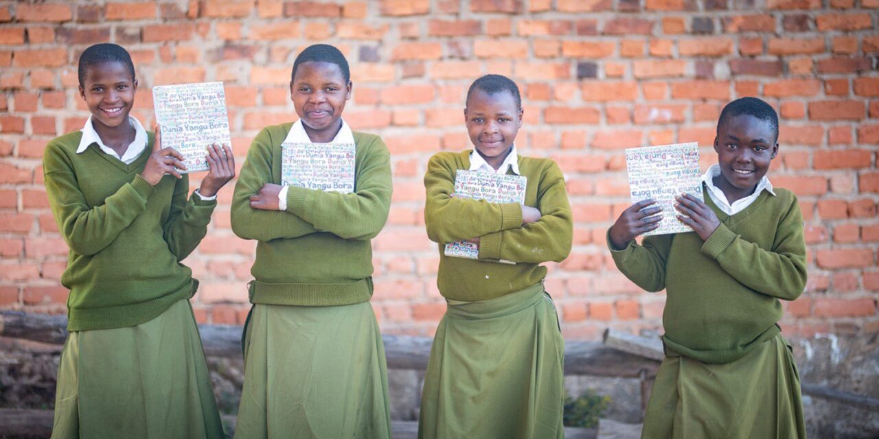 Students Hadija, Anna, Maria, and Jesca holding their My Better World self-development books outside their school in Tanzania’s Kilolo district.