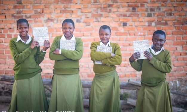 Students Hadija, Anna, Maria, and Jesca holding their My Better World self-development books outside their school in Tanzania’s Kilolo district.