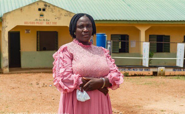 Nigerian women teacher stands in the playground outside her classroom.