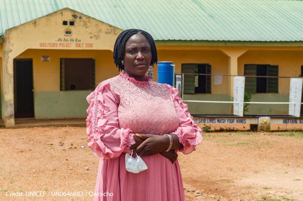 Nigerian women teacher stands in the playground outside her classroom.