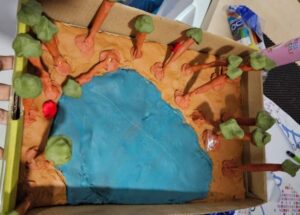 Model of a lake with trees around made by children using paper and paint 