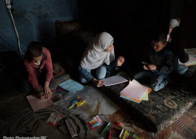 Children and a caregiver implement the remote early learning program at home on a carpet on the floor of a dark room with poor evening light.