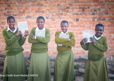 4 girl Students Hadija, Anna, Maria, and Jesca wearing green uniform and holding their My Better World self-development books outside their school in Tanzania’s Kilolo district.