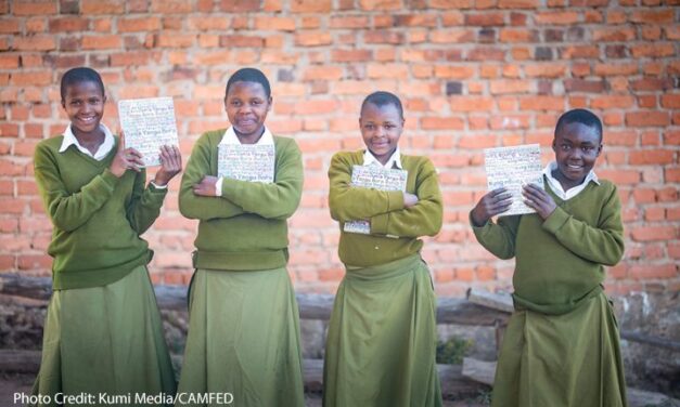 4 girl Students Hadija, Anna, Maria, and Jesca wearing green uniform and holding their My Better World self-development books outside their school in Tanzania’s Kilolo district.