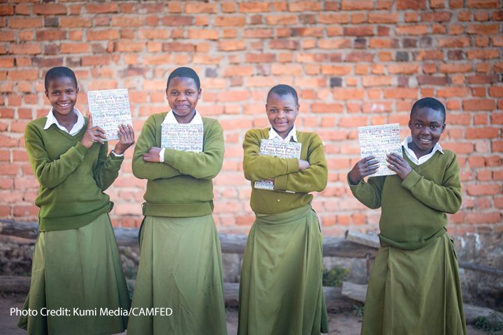 4 girl Students Hadija, Anna, Maria, and Jesca wearing green uniform and holding their My Better World self-development books outside their school in Tanzania’s Kilolo district.