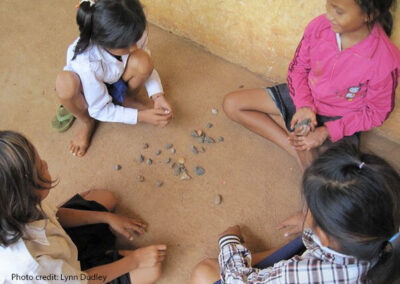 Four young girls play with little stones outside their school in Cambodia.