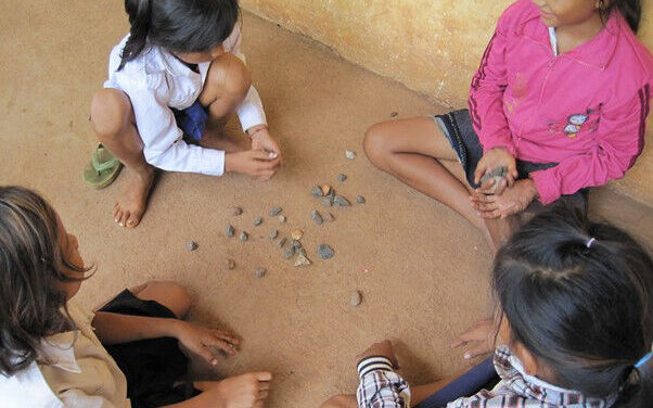 Four young girls play with little stones outside their school in Cambodia.