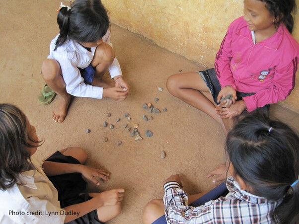 Four young girls play with little stones outside their school in Cambodia.