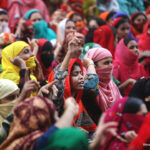 Indian women protesting. Wearing brightly coloured clothes, some with hand raised.