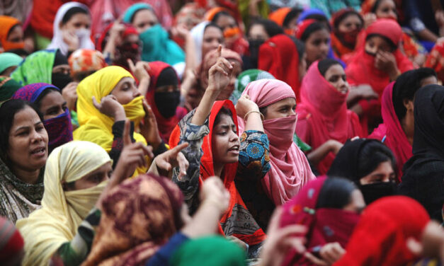 Indian women protesting. Wearing brightly coloured clothes, some with hand raised.