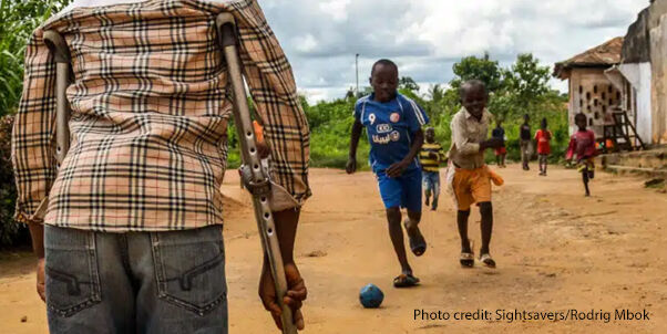 View from behind a child on crutches, watching his friends play at a Sightsavers supported inclusive school in Cameroon.