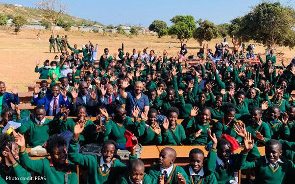 Children waving and wearing green uniform at the new Mushili Hillside secondary school celebrate outside with the Zambia Minister of Education and the UK Foreign Secretary.