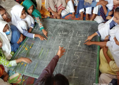 A para-teacher in Shikarpur using fallen leaves to teach his class the concept of ones and tens on a chalk board laid flat