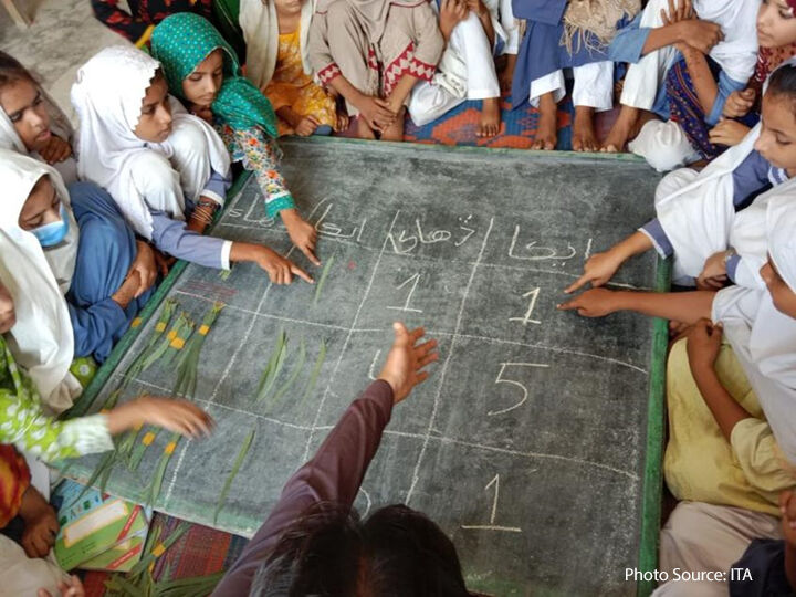 A para-teacher in Shikarpur using fallen leaves to teach his class the concept of ones and tens on a chalk board laid flat