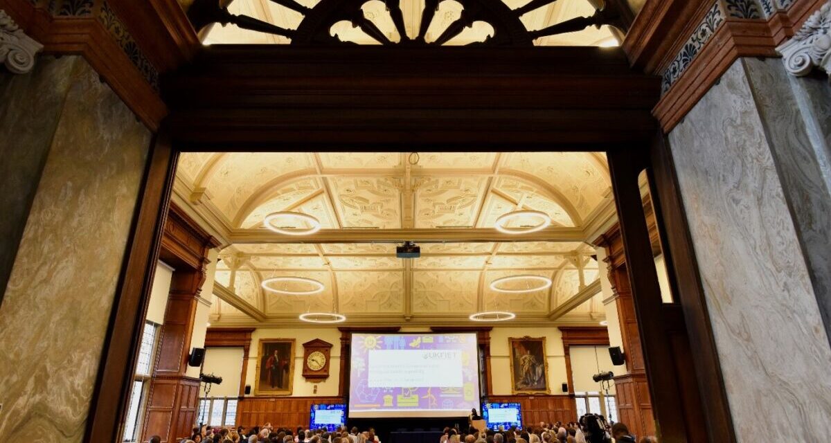 A view from the back of the room towards the screen in the UKFIET 2023 closing plenary. Picture also shows the arched window above the doorway and the ornate ceiling